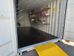 Organized shipping container with installed shelving, labeled storage boxes, and a yellow ramp for easy access—demonstrating how to organize a shipping container efficiently.