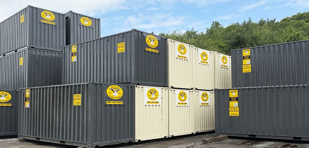 Black and tan Eagle Leasing branded storage containers stacked in a yard.